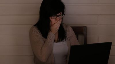 Verleumdung - Frau sitzt erschrocken am Computer